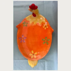 Κεραμική πιατέλα σε σχήμα μιας χαρούμενης κότας σε έντονο πορτοκαλί χρώμα, στολισμένη με κίτρινα και πράσινα λουλούδια